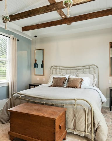 Bedroom with metal bed frame, exposed wood beams, blue-green accent wall, and cream curtains
