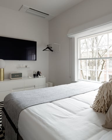 Modern bedroom with wall-mounted TV, white dresser, large window with city view, and striped area rug