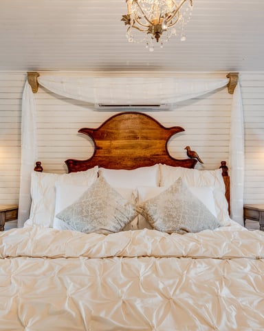 Bedroom with wooden four-poster bed, cream bedding, white shiplap walls, brass chandelier, and green lantern sconces