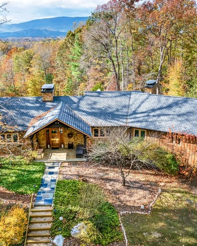 Modern stone and wood house with slate roof nestled in autumn forest, mountain view in distance