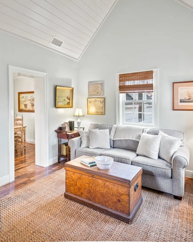 Bright living room with gray sofa, wooden chest coffee table, framed nautical artwork, and skylight ceiling