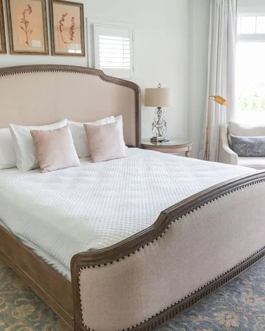Bright bedroom with upholstered bed, large windows, seating area, and botanical wall art
