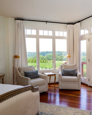 Bedroom with hardwood floors, upholstered bed, two armchairs, and French doors opening to vineyard views